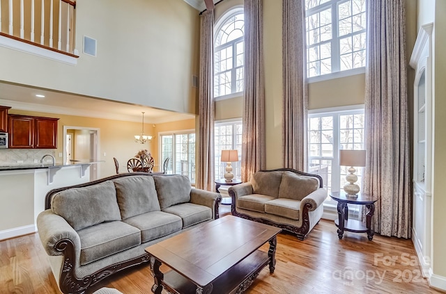 living room featuring light wood finished floors, a high ceiling, visible vents, and a notable chandelier