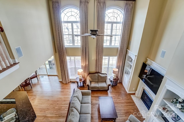 living room featuring a towering ceiling, plenty of natural light, a fireplace with flush hearth, and wood finished floors