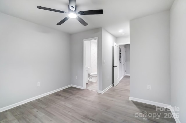 unfurnished bedroom featuring a ceiling fan, ensuite bath, baseboards, and wood finished floors