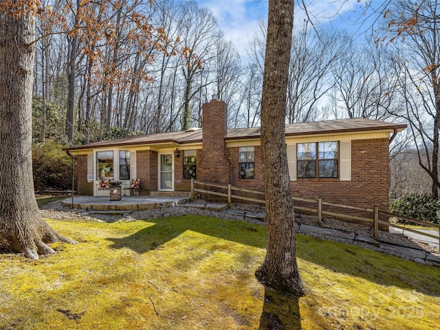 ranch-style house featuring brick siding, a chimney, a patio area, fence, and a front lawn