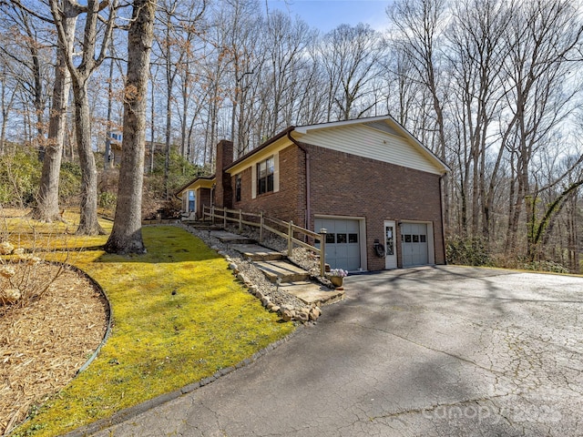 view of side of property featuring aphalt driveway, brick siding, a chimney, a lawn, and an attached garage