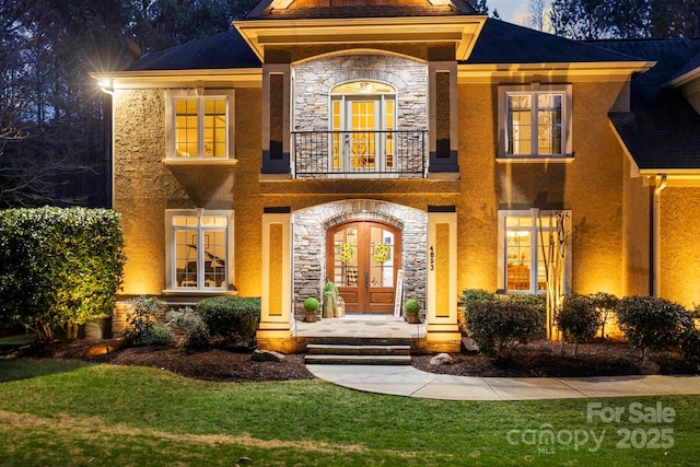 view of front facade featuring a balcony, stone siding, stucco siding, and french doors