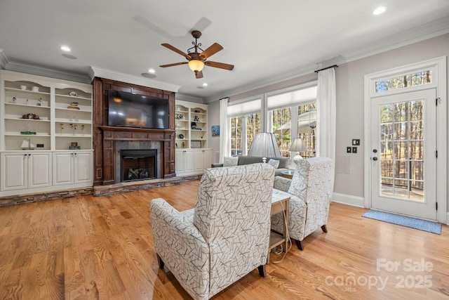 living area with light wood finished floors, a large fireplace, ornamental molding, and recessed lighting