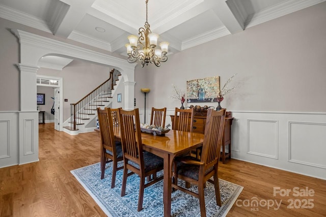 dining room featuring arched walkways, beamed ceiling, stairs, and decorative columns