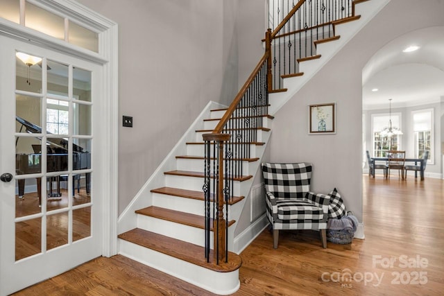 staircase with an inviting chandelier, arched walkways, and wood finished floors