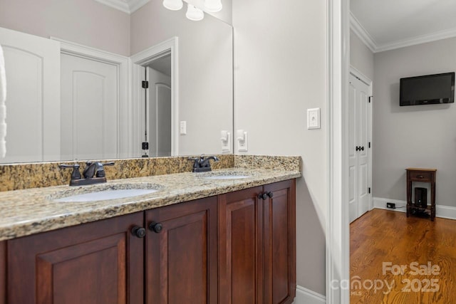 bathroom with crown molding, double vanity, a sink, and wood finished floors