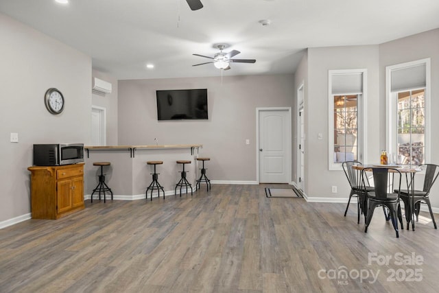 interior space featuring stainless steel microwave, wood finished floors, a wall mounted AC, and baseboards