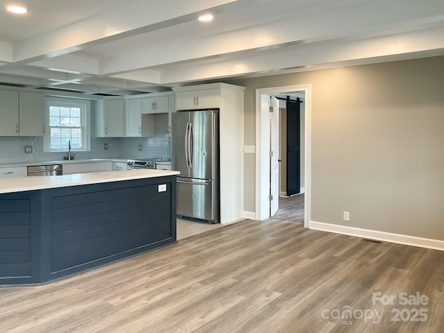 kitchen featuring light wood-type flooring, a barn door, appliances with stainless steel finishes, and light countertops