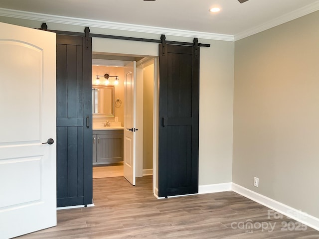 unfurnished bedroom with a barn door, ornamental molding, and light wood-style flooring