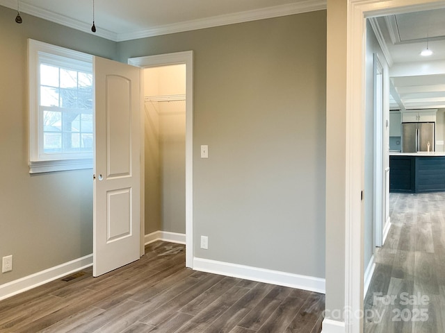 unfurnished bedroom featuring dark wood-style floors, crown molding, attic access, freestanding refrigerator, and baseboards