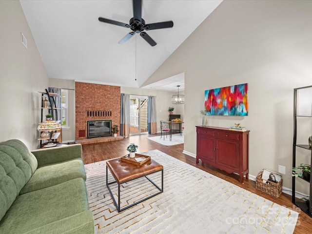 living room with visible vents, a brick fireplace, baseboards, ceiling fan with notable chandelier, and wood finished floors