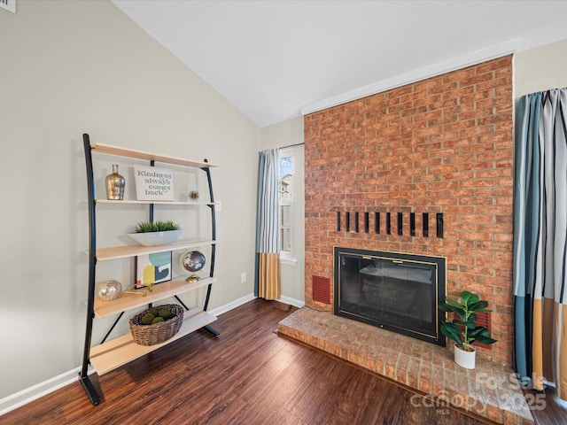 living room featuring vaulted ceiling, a brick fireplace, wood finished floors, and baseboards