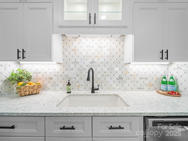 kitchen with a sink, backsplash, light stone countertops, and stainless steel dishwasher