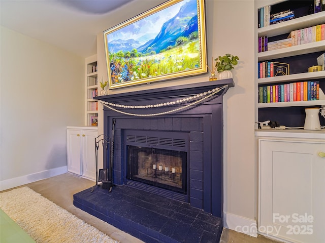 room details featuring a fireplace with raised hearth, baseboards, and built in features