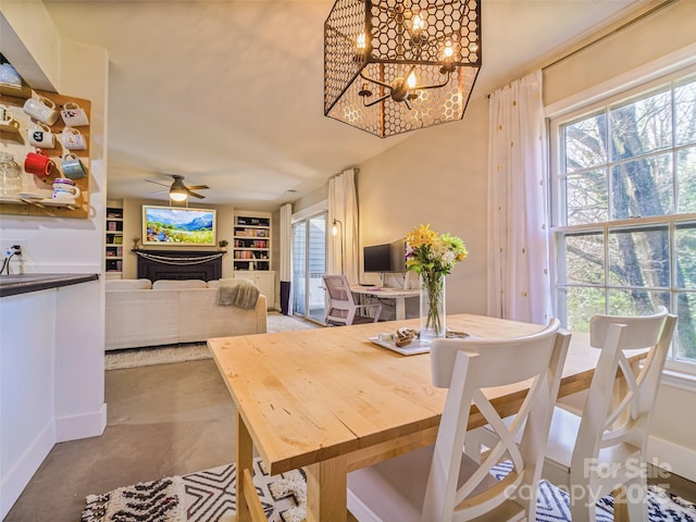 dining space featuring built in features, a wealth of natural light, concrete flooring, and ceiling fan with notable chandelier