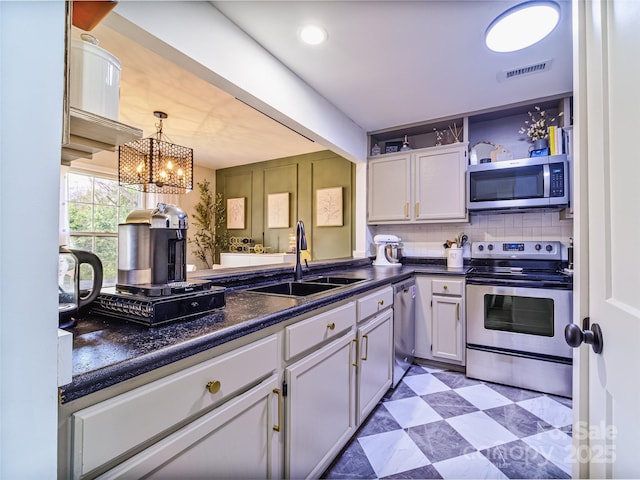 kitchen with light floors, stainless steel appliances, dark countertops, visible vents, and a sink