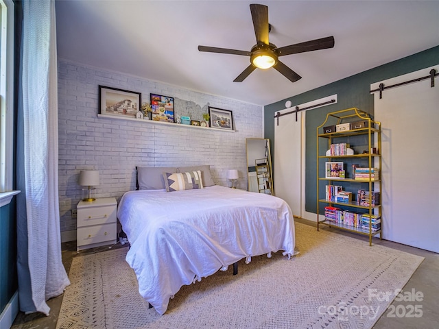 bedroom with a ceiling fan, brick wall, and a barn door