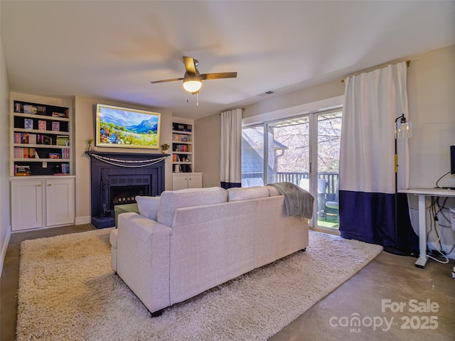 living area with visible vents, a fireplace with raised hearth, a ceiling fan, built in shelves, and concrete floors