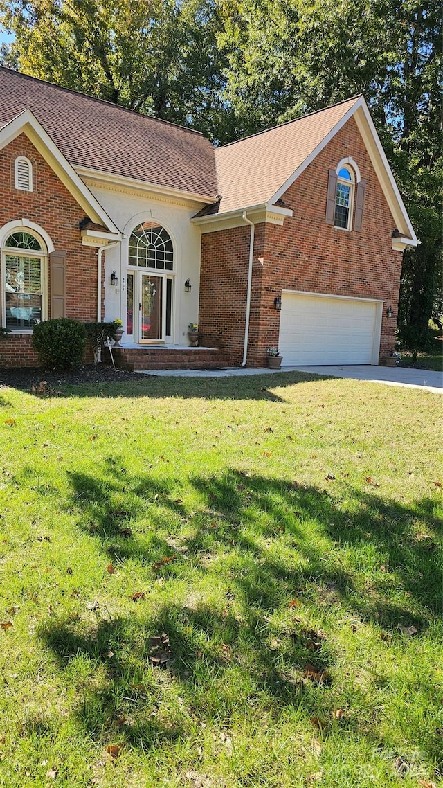 view of front of house featuring brick siding, roof with shingles, stucco siding, a front yard, and a garage