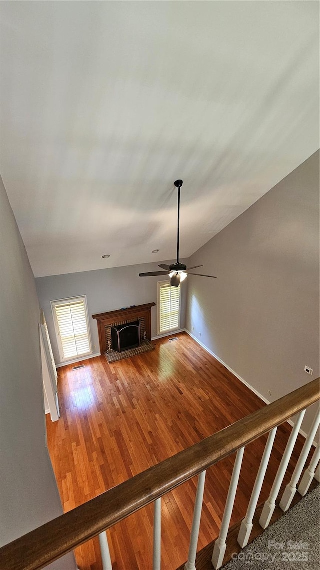 unfurnished living room featuring lofted ceiling, visible vents, stairway, a brick fireplace, and hardwood / wood-style flooring