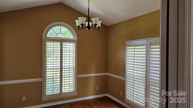 empty room with dark wood finished floors, lofted ceiling, visible vents, a chandelier, and baseboards