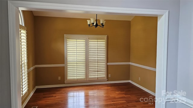 spare room with baseboards, wood finished floors, and a notable chandelier