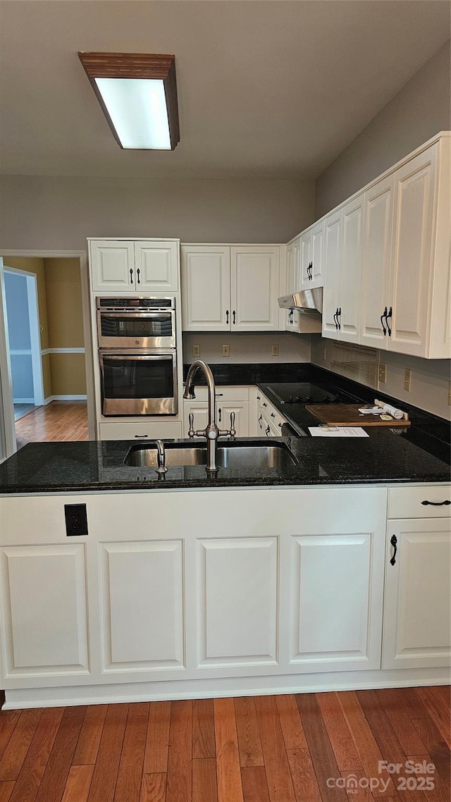 kitchen featuring double oven, white cabinets, a sink, and under cabinet range hood