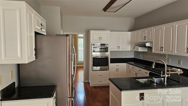 kitchen with dark wood-style flooring, appliances with stainless steel finishes, a sink, a peninsula, and under cabinet range hood