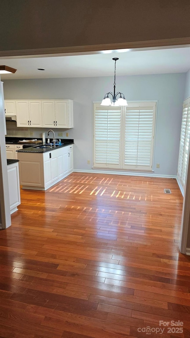 kitchen with visible vents, dark countertops, hardwood / wood-style floors, an inviting chandelier, and white cabinetry