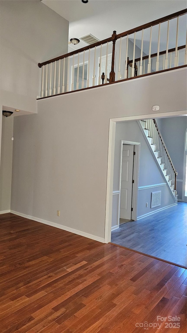 spare room featuring visible vents, stairway, a towering ceiling, wood finished floors, and baseboards