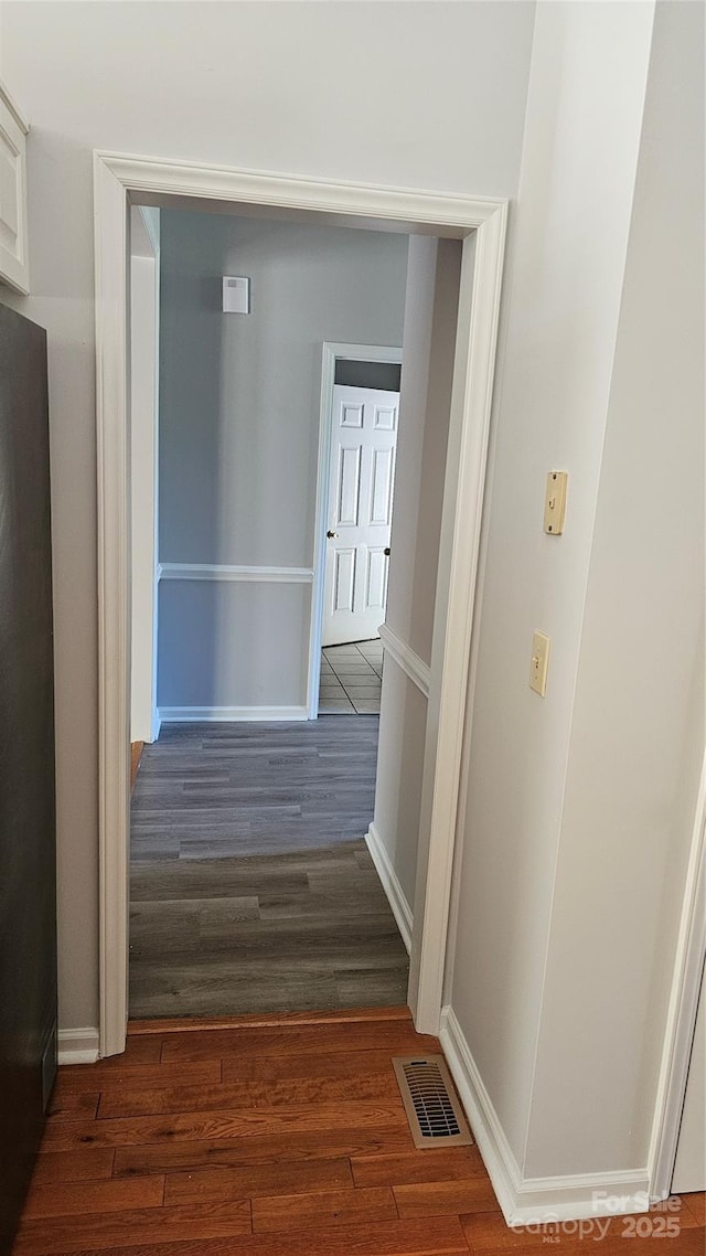 corridor featuring dark wood-style flooring, visible vents, and baseboards