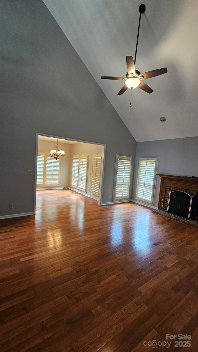 unfurnished living room with baseboards, wood finished floors, a fireplace, high vaulted ceiling, and ceiling fan with notable chandelier