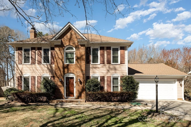 colonial-style house with a garage, brick siding, concrete driveway, a chimney, and a front yard