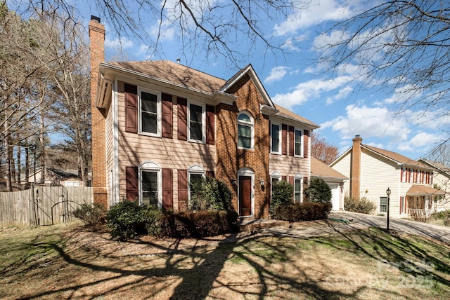 colonial-style house featuring a garage, a chimney, fence, and brick siding