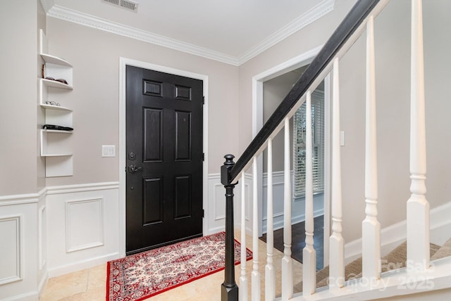 foyer with light tile patterned floors, wainscoting, stairway, ornamental molding, and a decorative wall