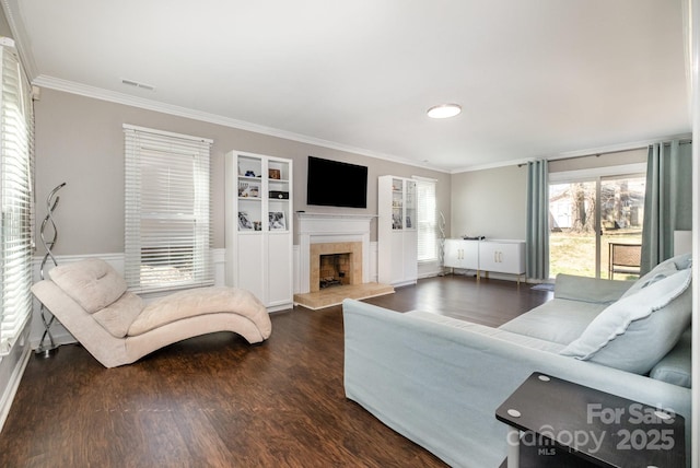 living area featuring built in features, visible vents, a tile fireplace, dark wood-type flooring, and crown molding