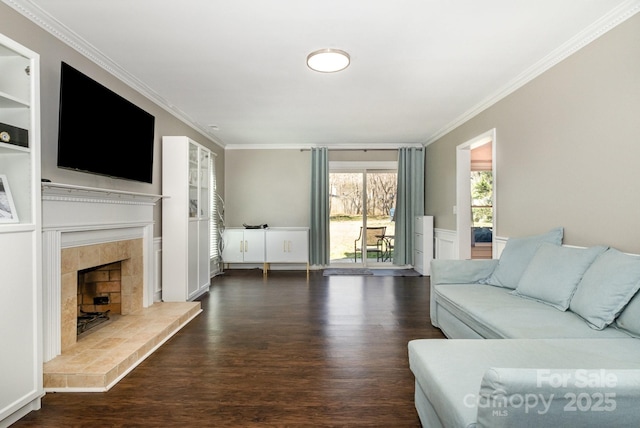 living room with ornamental molding, wainscoting, dark wood-type flooring, and a tiled fireplace