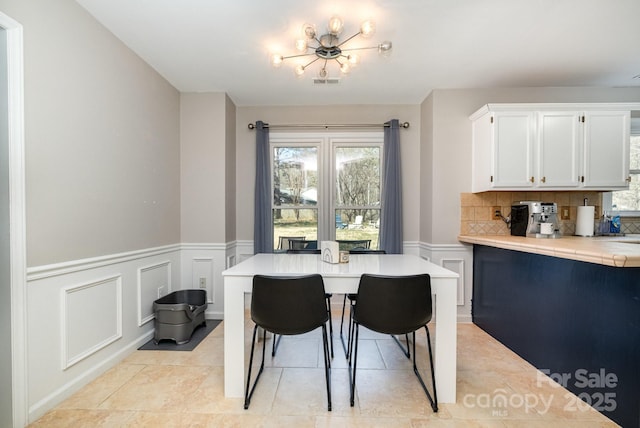 dining room with light tile patterned floors, wainscoting, visible vents, and a decorative wall