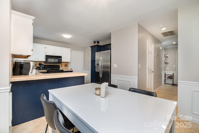 kitchen featuring visible vents, decorative backsplash, tile countertops, a peninsula, and black appliances