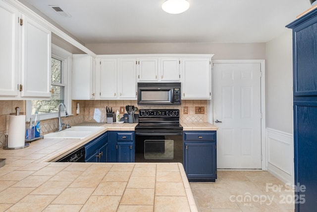 kitchen featuring tile countertops, blue cabinetry, black appliances, white cabinetry, and a sink