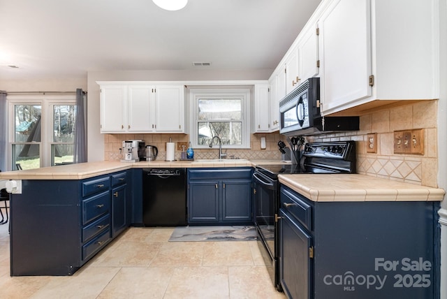 kitchen with a peninsula, black appliances, white cabinets, and a sink