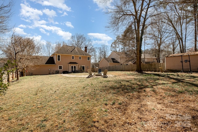 rear view of property with an outdoor fire pit, a lawn, a fenced backyard, a chimney, and an outdoor structure