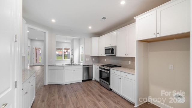 kitchen with light wood finished floors, visible vents, light stone countertops, stainless steel appliances, and a sink