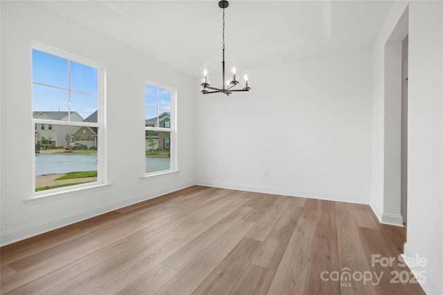 unfurnished dining area featuring light wood-style flooring, baseboards, and a notable chandelier