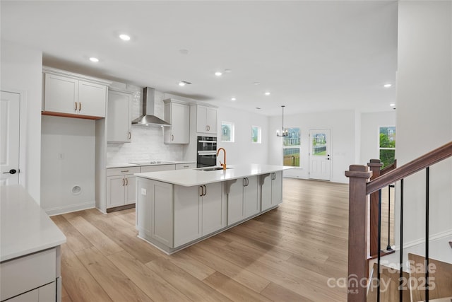 kitchen featuring tasteful backsplash, an island with sink, wall chimney exhaust hood, light countertops, and black appliances