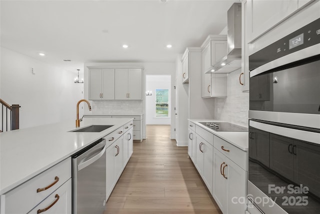 kitchen featuring stainless steel appliances, light countertops, a sink, light wood-type flooring, and wall chimney exhaust hood