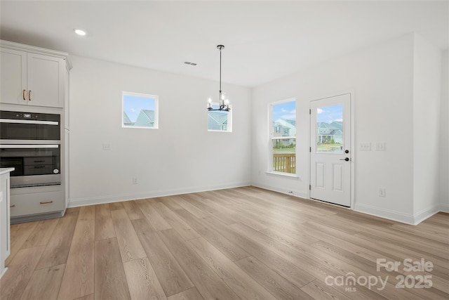 unfurnished dining area with light wood finished floors, an inviting chandelier, and a healthy amount of sunlight