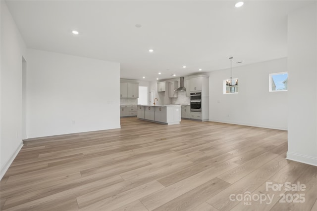 unfurnished living room with light wood-style flooring, a notable chandelier, recessed lighting, a sink, and baseboards