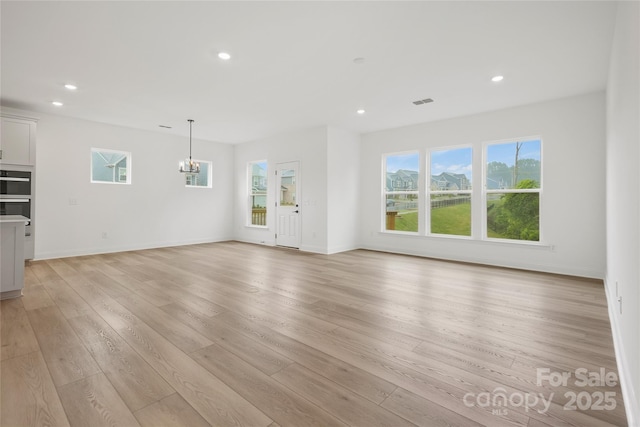 unfurnished living room with baseboards, an inviting chandelier, light wood-style flooring, and recessed lighting