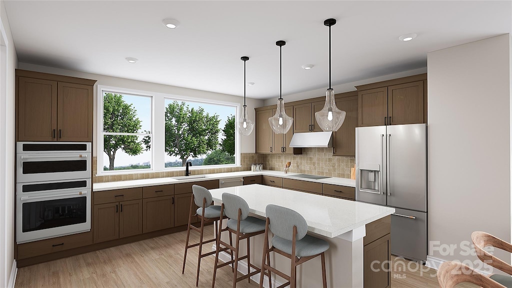 kitchen featuring under cabinet range hood, high end refrigerator, a sink, light countertops, and a center island